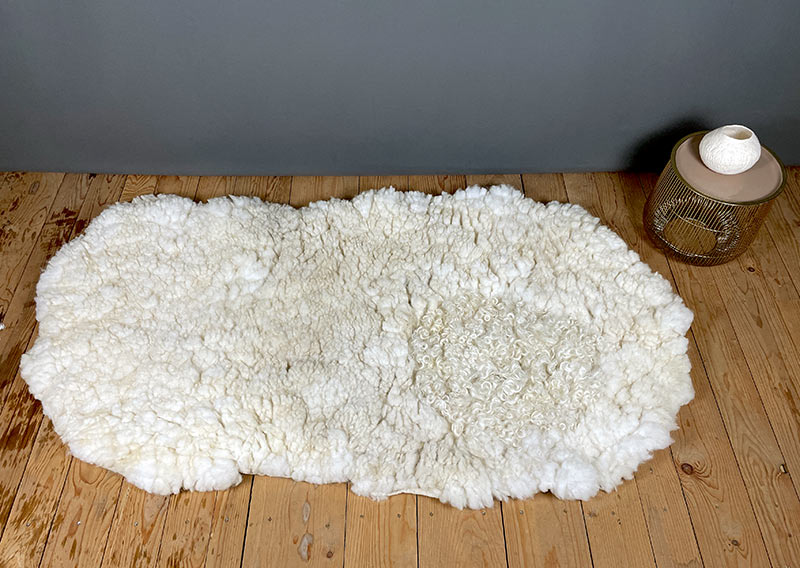 Die Liegewiese. 
Na, wenn das kein Prachtstück ist! Dieses Filzfell misst stattliche 1,75 × 1 Meter – das grösste, das je die Werkstatt der Fellfilzerei Jawoll verlassen hat.
Gefertigt aus feinster Romney-Wolle in Schafsmilchweiss, kräftig und weich zugleich, und veredelt mit einem Kreis aus Locken der Walliser Schwarznasenschafe – als wäre ein Stück Alpenpoesie eingefilzt.

Mehrere Schafe aus dem Kanton Bern haben hier ihre Wolle gespendet – und das Ergebnis ist einfach jawollig schön. Dieses Fell ist so dick, weich und robust, dass es fast schon nach draussen ruft: „Mach’s dir gemütlich!“

Ob auf dem grossen Sofa, im Bett oder direkt auf dem Boden – diese Liegewiese lädt zum Lesen, Träumen und Musiklauschen ein. Kinder lieben sie genauso wie Erwachsene, die sich zwischendurch eine sanfte Wolke unterlegen möchten.

Ein echtes Unikat – und ja, das darf man diesem Wunderwerk auch im Preis ansehen.
Mit einem Augenzwinkern: So ein Stück entsteht wohl nur einmal im Leben …