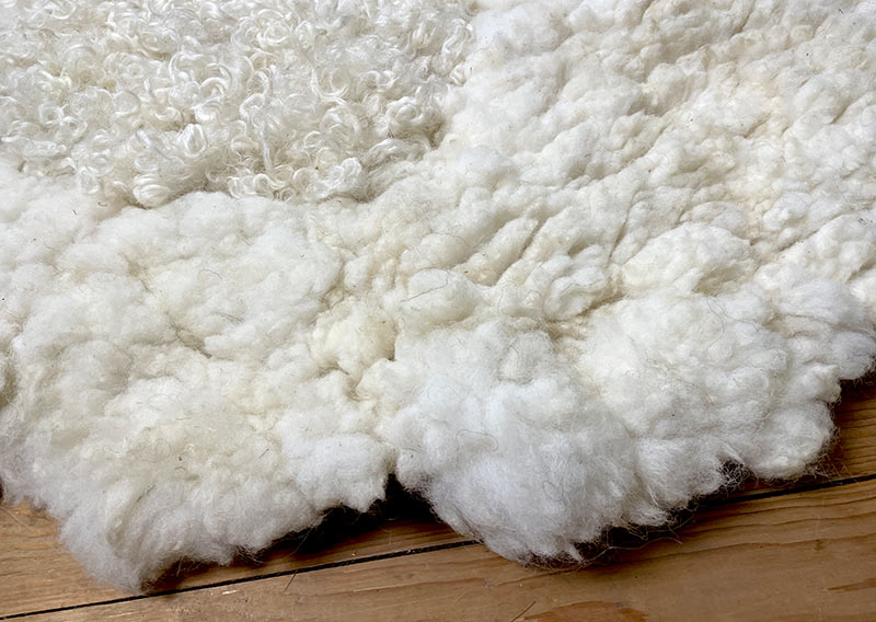 Die Liegewiese. 
Na, wenn das kein Prachtstück ist! Dieses Filzfell misst stattliche 1,75 × 1 Meter – das grösste, das je die Werkstatt der Fellfilzerei Jawoll verlassen hat.
Gefertigt aus feinster Romney-Wolle in Schafsmilchweiss, kräftig und weich zugleich, und veredelt mit einem Kreis aus Locken der Walliser Schwarznasenschafe – als wäre ein Stück Alpenpoesie eingefilzt.

Mehrere Schafe aus dem Kanton Bern haben hier ihre Wolle gespendet – und das Ergebnis ist einfach jawollig schön. Dieses Fell ist so dick, weich und robust, dass es fast schon nach draussen ruft: „Mach’s dir gemütlich!“

Ob auf dem grossen Sofa, im Bett oder direkt auf dem Boden – diese Liegewiese lädt zum Lesen, Träumen und Musiklauschen ein. Kinder lieben sie genauso wie Erwachsene, die sich zwischendurch eine sanfte Wolke unterlegen möchten.

Ein echtes Unikat – und ja, das darf man diesem Wunderwerk auch im Preis ansehen.
Mit einem Augenzwinkern: So ein Stück entsteht wohl nur einmal im Leben …