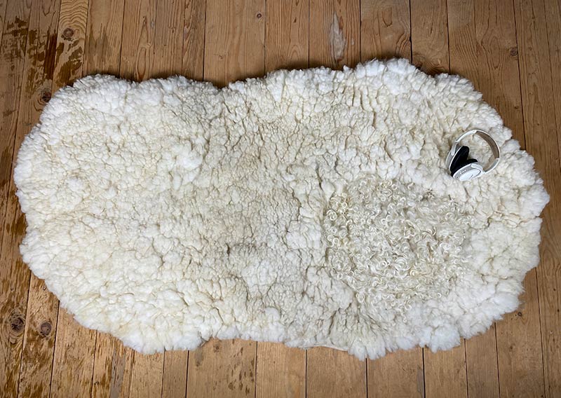 Die Liegewiese. 
Na, wenn das kein Prachtstück ist! Dieses Filzfell misst stattliche 1,75 × 1 Meter – das grösste, das je die Werkstatt der Fellfilzerei Jawoll verlassen hat.
Gefertigt aus feinster Romney-Wolle in Schafsmilchweiss, kräftig und weich zugleich, und veredelt mit einem Kreis aus Locken der Walliser Schwarznasenschafe – als wäre ein Stück Alpenpoesie eingefilzt.

Mehrere Schafe aus dem Kanton Bern haben hier ihre Wolle gespendet – und das Ergebnis ist einfach jawollig schön. Dieses Fell ist so dick, weich und robust, dass es fast schon nach draussen ruft: „Mach’s dir gemütlich!“

Ob auf dem grossen Sofa, im Bett oder direkt auf dem Boden – diese Liegewiese lädt zum Lesen, Träumen und Musiklauschen ein. Kinder lieben sie genauso wie Erwachsene, die sich zwischendurch eine sanfte Wolke unterlegen möchten.

Ein echtes Unikat – und ja, das darf man diesem Wunderwerk auch im Preis ansehen.
Mit einem Augenzwinkern: So ein Stück entsteht wohl nur einmal im Leben …