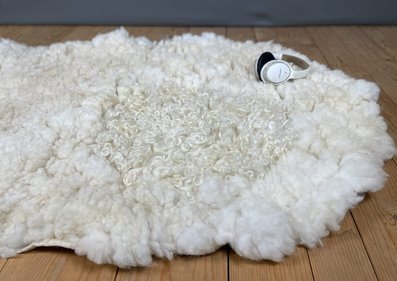 Die Liegewiese. 
Na, wenn das kein Prachtstück ist! Dieses Filzfell misst stattliche 1,75 × 1 Meter – das grösste, das je die Werkstatt der Fellfilzerei Jawoll verlassen hat.
Gefertigt aus feinster Romney-Wolle in Schafsmilchweiss, kräftig und weich zugleich, und veredelt mit einem Kreis aus Locken der Walliser Schwarznasenschafe – als wäre ein Stück Alpenpoesie eingefilzt.

Mehrere Schafe aus dem Kanton Bern haben hier ihre Wolle gespendet – und das Ergebnis ist einfach jawollig schön. Dieses Fell ist so dick, weich und robust, dass es fast schon nach draussen ruft: „Mach’s dir gemütlich!“

Ob auf dem grossen Sofa, im Bett oder direkt auf dem Boden – diese Liegewiese lädt zum Lesen, Träumen und Musiklauschen ein. Kinder lieben sie genauso wie Erwachsene, die sich zwischendurch eine sanfte Wolke unterlegen möchten.

Ein echtes Unikat – und ja, das darf man diesem Wunderwerk auch im Preis ansehen.
Mit einem Augenzwinkern: So ein Stück entsteht wohl nur einmal im Leben …