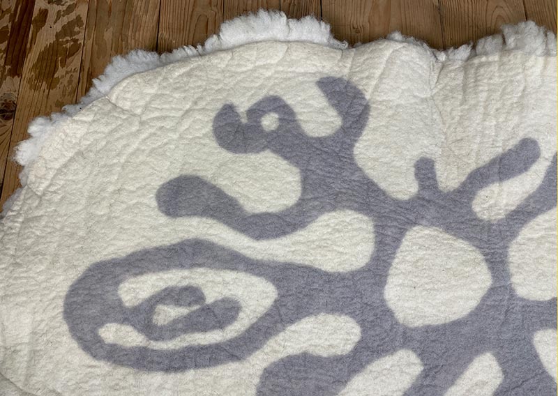 Die Liegewiese. 
Na, wenn das kein Prachtstück ist! Dieses Filzfell misst stattliche 1,75 × 1 Meter – das grösste, das je die Werkstatt der Fellfilzerei Jawoll verlassen hat.
Gefertigt aus feinster Romney-Wolle in Schafsmilchweiss, kräftig und weich zugleich, und veredelt mit einem Kreis aus Locken der Walliser Schwarznasenschafe – als wäre ein Stück Alpenpoesie eingefilzt.

Mehrere Schafe aus dem Kanton Bern haben hier ihre Wolle gespendet – und das Ergebnis ist einfach jawollig schön. Dieses Fell ist so dick, weich und robust, dass es fast schon nach draussen ruft: „Mach’s dir gemütlich!“

Ob auf dem grossen Sofa, im Bett oder direkt auf dem Boden – diese Liegewiese lädt zum Lesen, Träumen und Musiklauschen ein. Kinder lieben sie genauso wie Erwachsene, die sich zwischendurch eine sanfte Wolke unterlegen möchten.

Ein echtes Unikat – und ja, das darf man diesem Wunderwerk auch im Preis ansehen.
Mit einem Augenzwinkern: So ein Stück entsteht wohl nur einmal im Leben …