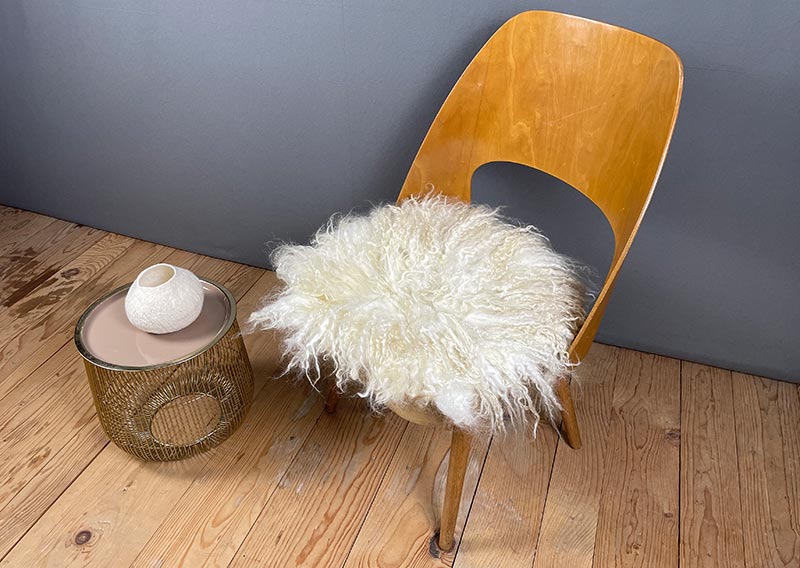 Sonnenaufgangsweiss – Sitzfell vom Walliser Schwarznasen-Schaf.
Ein bisschen wild darf’s schon sein. Dieses Fell vom Walliser Schwarznasen-Schaf bringt genau das mit: Locken, Zotteln und Charakter. Die Fasern sind unterschiedlich lang – bis zu 20 cm –, und jede Strähne scheint ihre eigene kleine Geschichte zu erzählen.

Gefilzt aus Wolle einer alten Walliser Rasse, die dort oben zwischen Felsen und Sonne zuhause ist. Wetterfest, robust und doch erstaunlich weich – so wie das Land, aus dem sie stammt.

Mit seinem grösseren Durchmesser (ca. 48 cm) passt dieses Sonnenaufgangsweiss-Fell wunderbar auf Sessel oder Stühle mit etwas mehr Platz.
Ein Stück Morgenglanz aus den Bergen – zum Sitzen, Durchatmen und die Gedanken schweifen lassen.