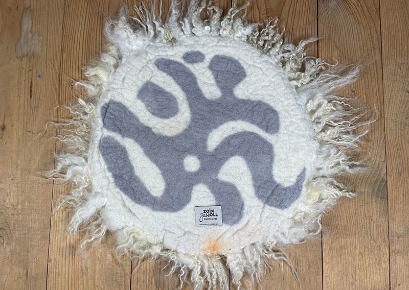 Sonnenaufgangsweiss – Sitzfell vom Walliser Schwarznasen-Schaf.
Ein bisschen wild darf’s schon sein. Dieses Fell vom Walliser Schwarznasen-Schaf bringt genau das mit: Locken, Zotteln und Charakter. Die Fasern sind unterschiedlich lang – bis zu 20 cm –, und jede Strähne scheint ihre eigene kleine Geschichte zu erzählen.

Gefilzt aus Wolle einer alten Walliser Rasse, die dort oben zwischen Felsen und Sonne zuhause ist. Wetterfest, robust und doch erstaunlich weich – so wie das Land, aus dem sie stammt.

Mit seinem grösseren Durchmesser (ca. 48 cm) passt dieses Sonnenaufgangsweiss-Fell wunderbar auf Sessel oder Stühle mit etwas mehr Platz.
Ein Stück Morgenglanz aus den Bergen – zum Sitzen, Durchatmen und die Gedanken schweifen lassen.